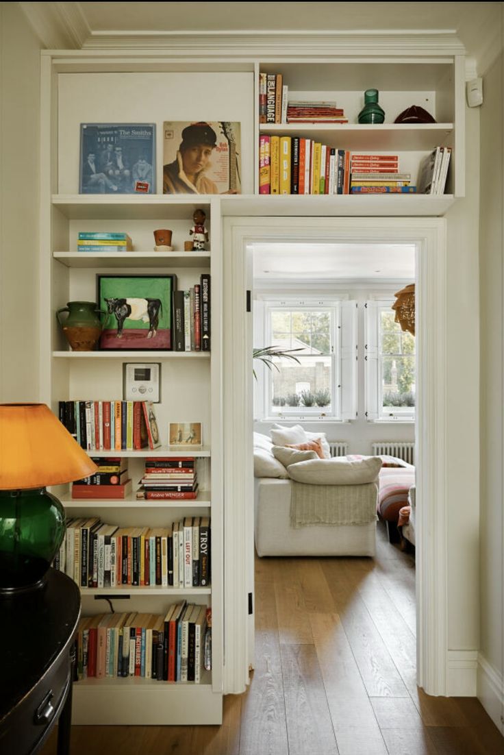 a living room filled with lots of books on top of a white book shelf next to a window