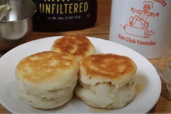 two biscuits on a white plate next to a cup of coffee and a shaker