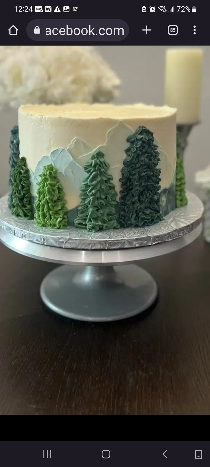 a cake decorated with pine trees on top of a wooden table next to a candle