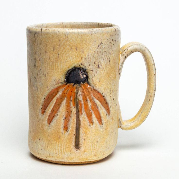 a ceramic mug with an orange and black flower on it's side, sitting on a white surface