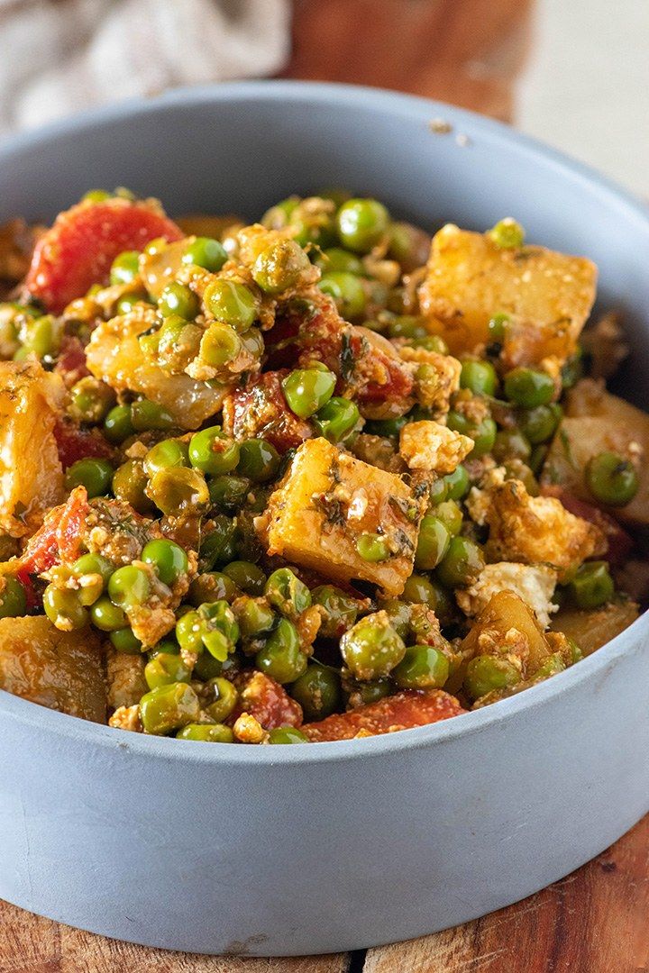 a blue bowl filled with peas and tofu on top of a wooden table next to a fork