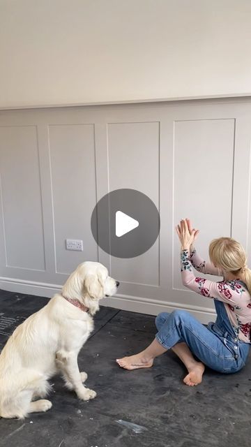 a woman sitting on the floor petting a white dog with her hand in it's mouth