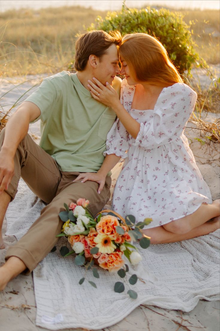 a man and woman are sitting on the beach with their arms around each other as they kiss