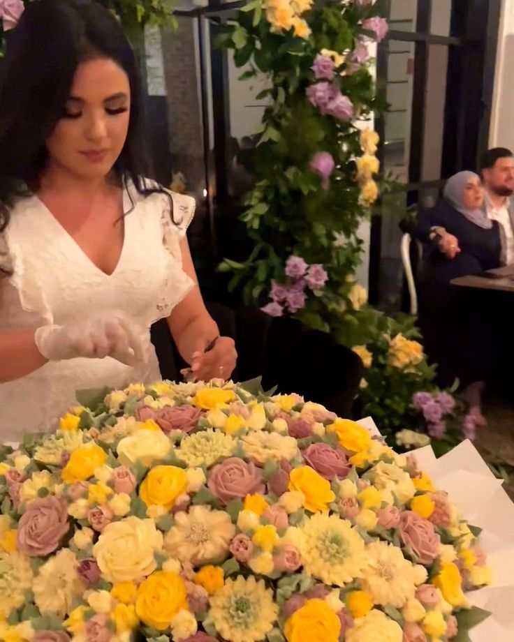 a woman in white dress cutting a cake with yellow and pink flowers