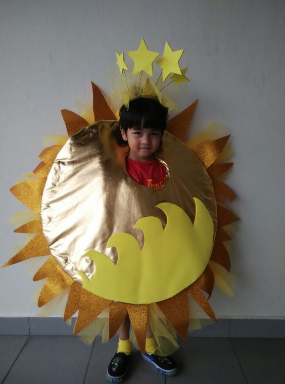 a young boy standing in front of a paper sun and moon costume on the wall