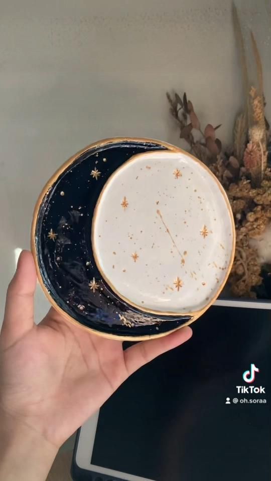 a hand is holding a blue and white plate with gold stars on it in front of a plant