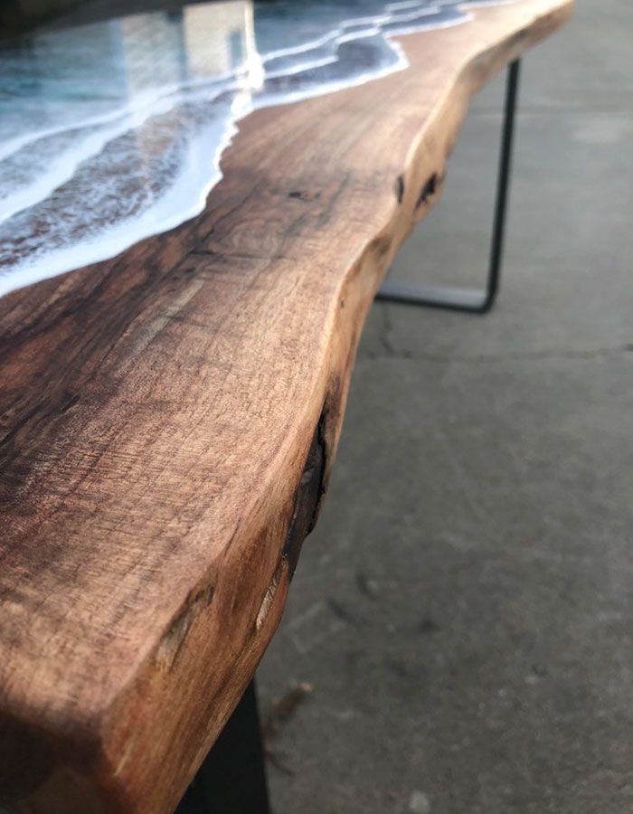 a close up of a wooden bench with water on it's surface and the ocean in the background