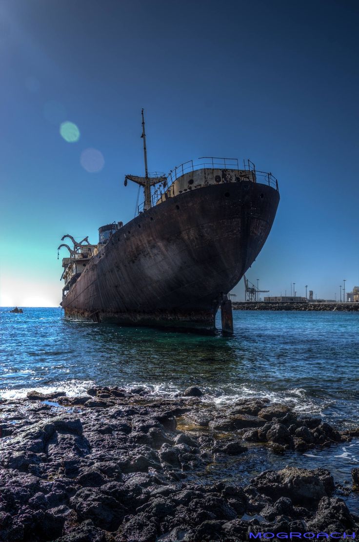 an old ship sitting on top of the ocean next to some rocks and water under a blue sky