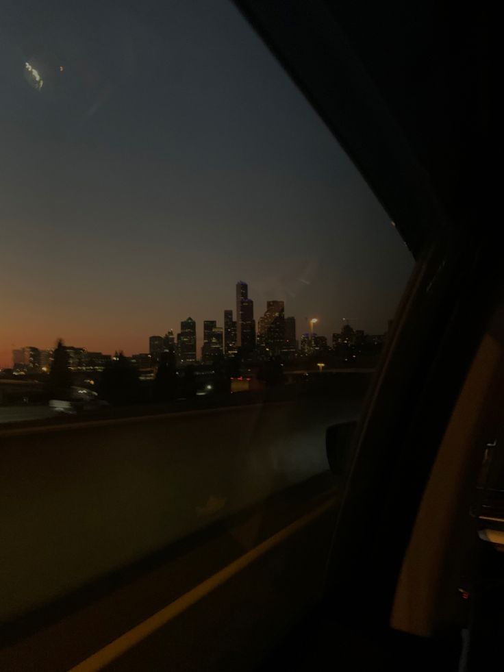 the sun is setting over a city skyline as seen from inside a car window with buildings in the background