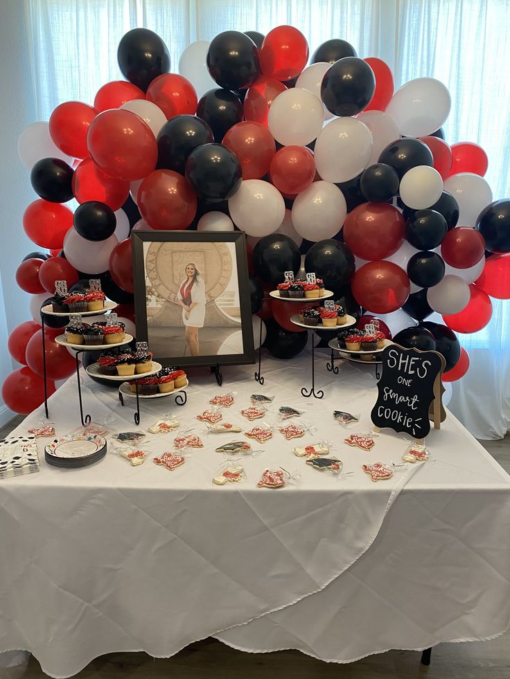 a table topped with cakes and balloons next to a framed photo on top of a white table cloth