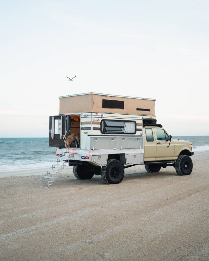 a truck with a camper attached to it parked on the beach next to the ocean