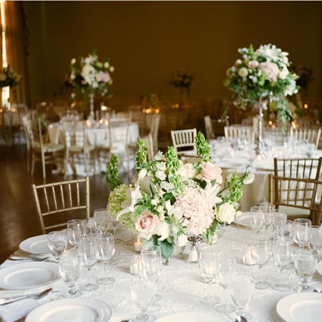 the table is set with white plates and silverware, flowers and greenery in vases