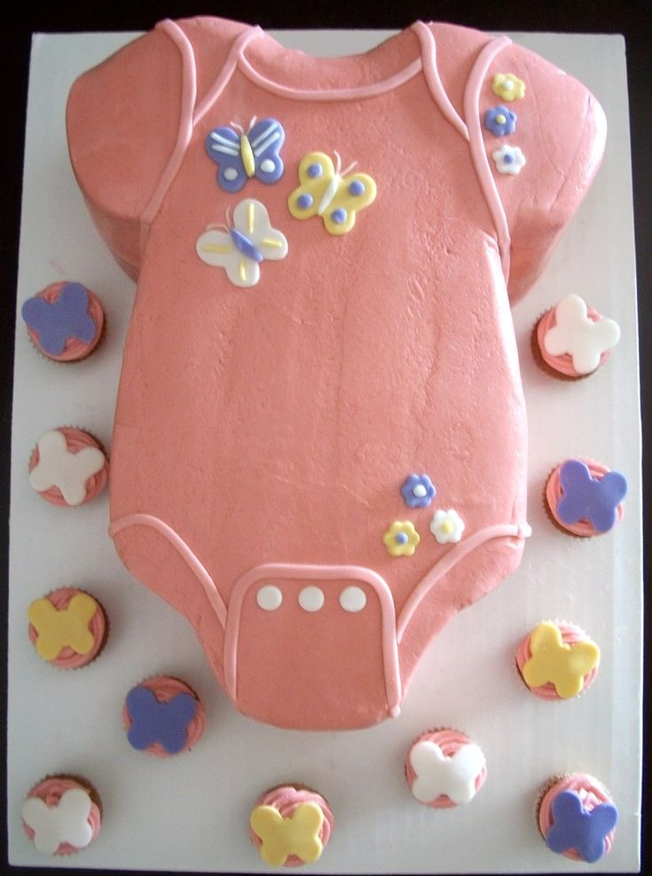 a cake shaped like a baby's bodysuit with cupcakes around it