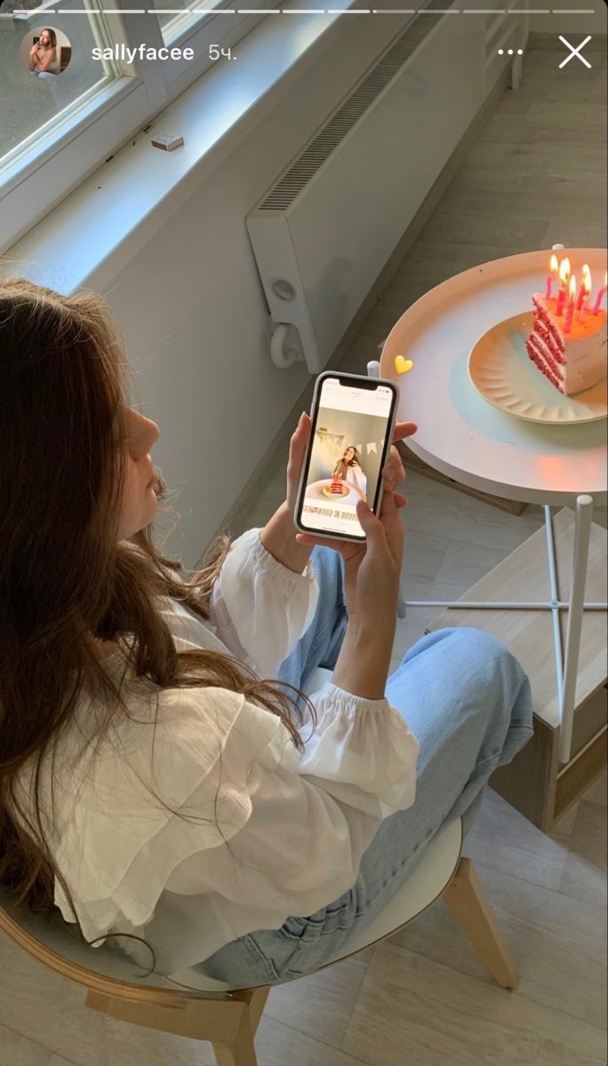 a woman sitting in a chair looking at her cell phone with candles on the table