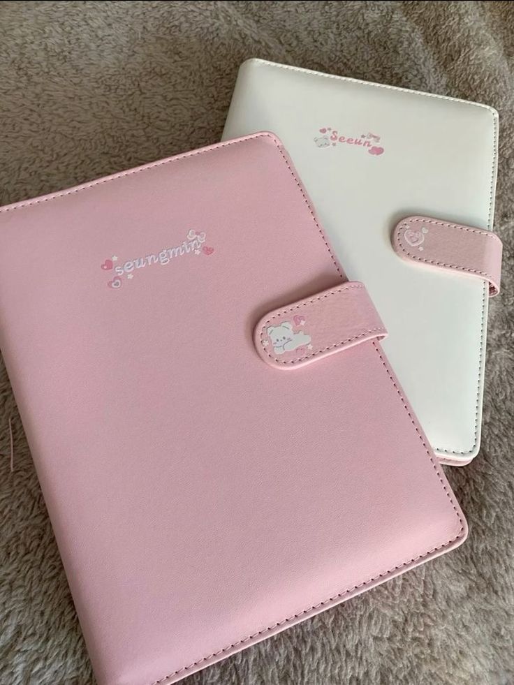 two pink and white notebooks sitting next to each other on a carpeted floor