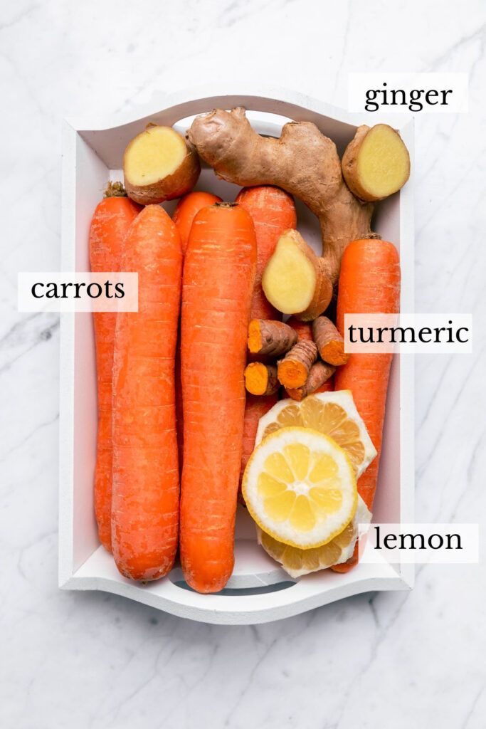 carrots, ginger, lemon and ginger root in a white tray on a marble surface