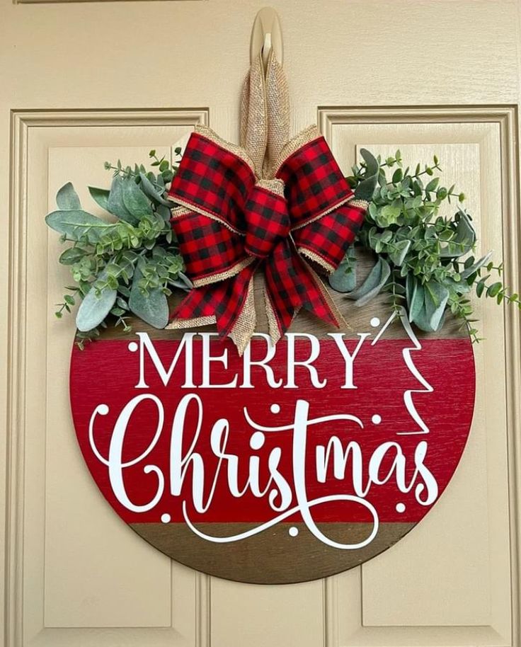 a merry christmas sign hanging on the front door with greenery and ribbon around it