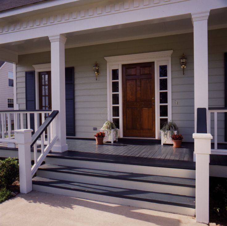 the front porch of a house with two potted plants on the steps and a wooden door