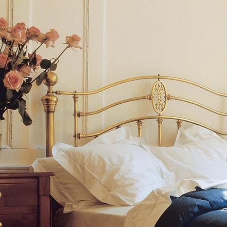 a bed with white sheets and pillows next to a vase full of flowers on top of it