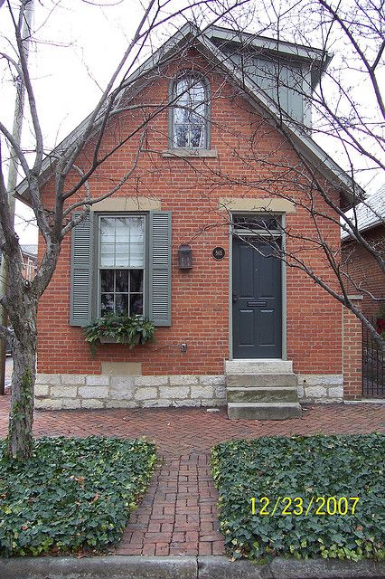 a red brick house with green shutters on the front and side windows, surrounded by greenery