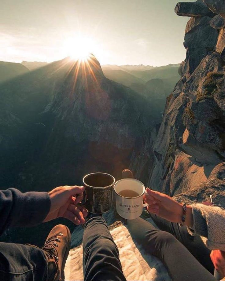 two people sitting on top of a mountain holding coffee cups