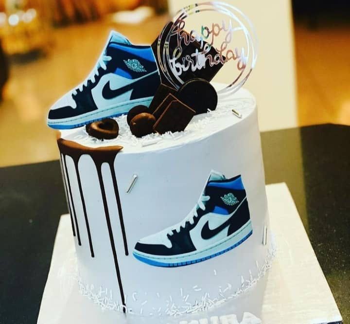 a white cake with blue and black nike shoes on top, sitting on a table