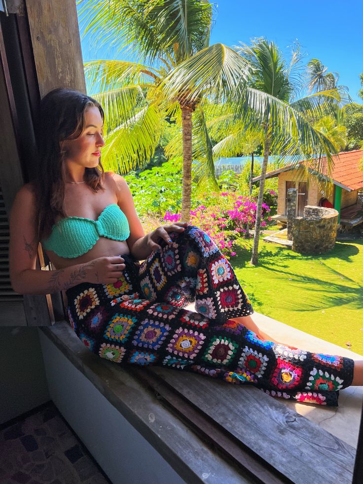 a woman sitting on a window sill with a blanket in front of her and palm trees behind her