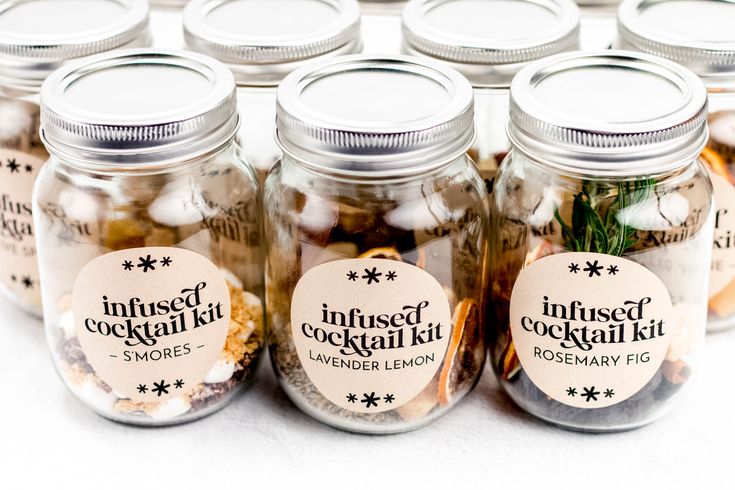 jars filled with different types of food on a white tableclothed surface and labeled infused cocktails