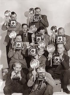 an old black and white photo of men holding up cameras with their heads in the air