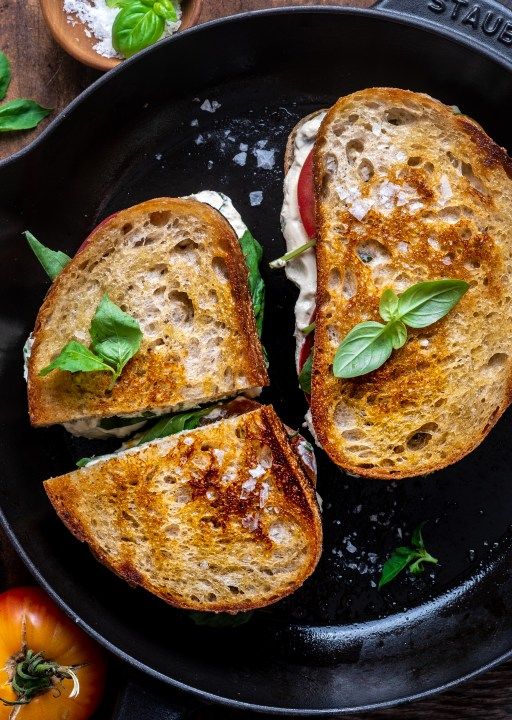 two slices of grilled cheese sandwich in a pan with basil and tomatoes on the side