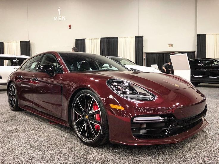 a red porsche panamer parked in a showroom with other cars behind it