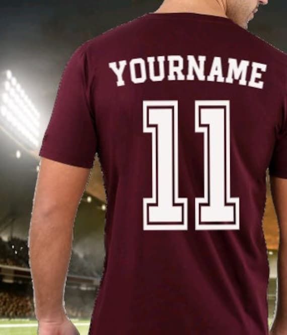 a man wearing a maroon shirt with the number 11 on it in front of a stadium