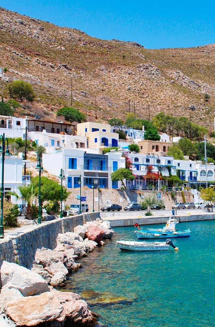 several boats are docked in the water near some buildings and hills with blue shuttered windows