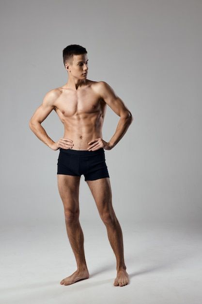 a man with no shirt standing in front of a gray background wearing black trunks and his hands on his hips