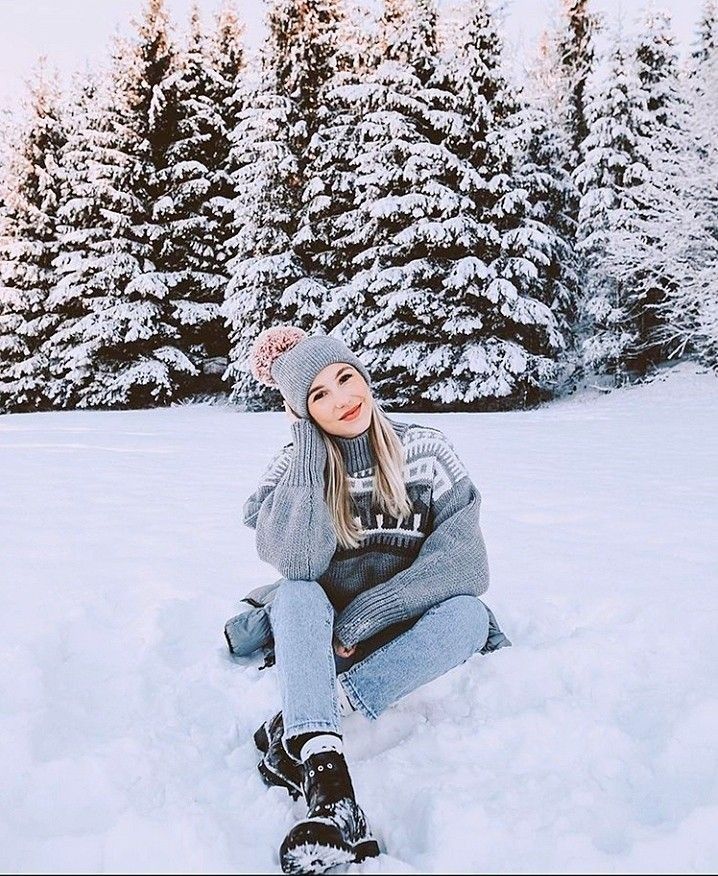 a woman sitting in the snow with her legs crossed and wearing a beanie hat