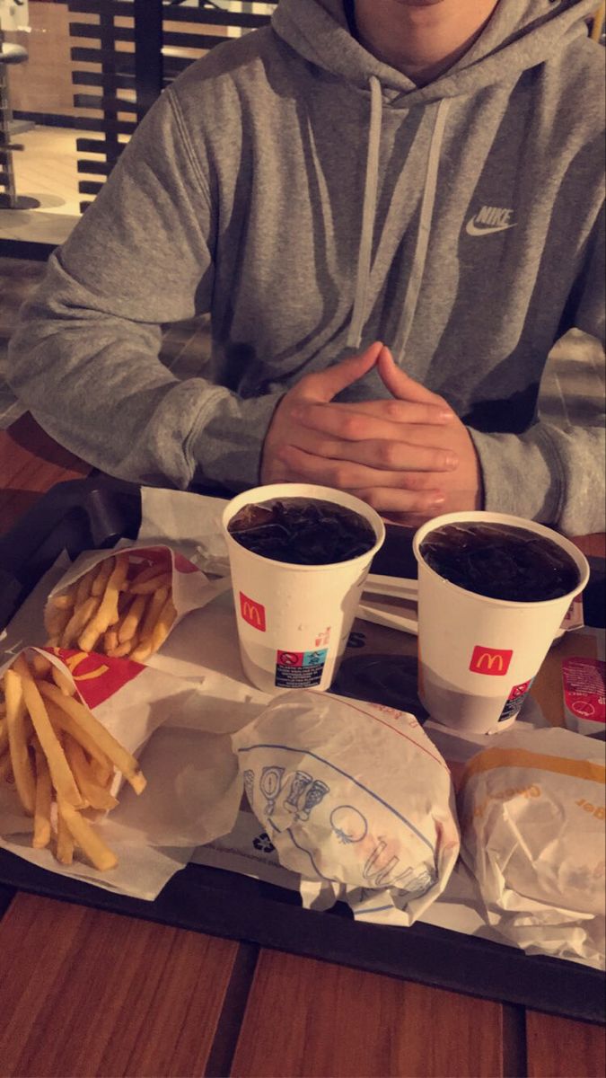 a man sitting at a table with two cups of coffee and french fries in front of him