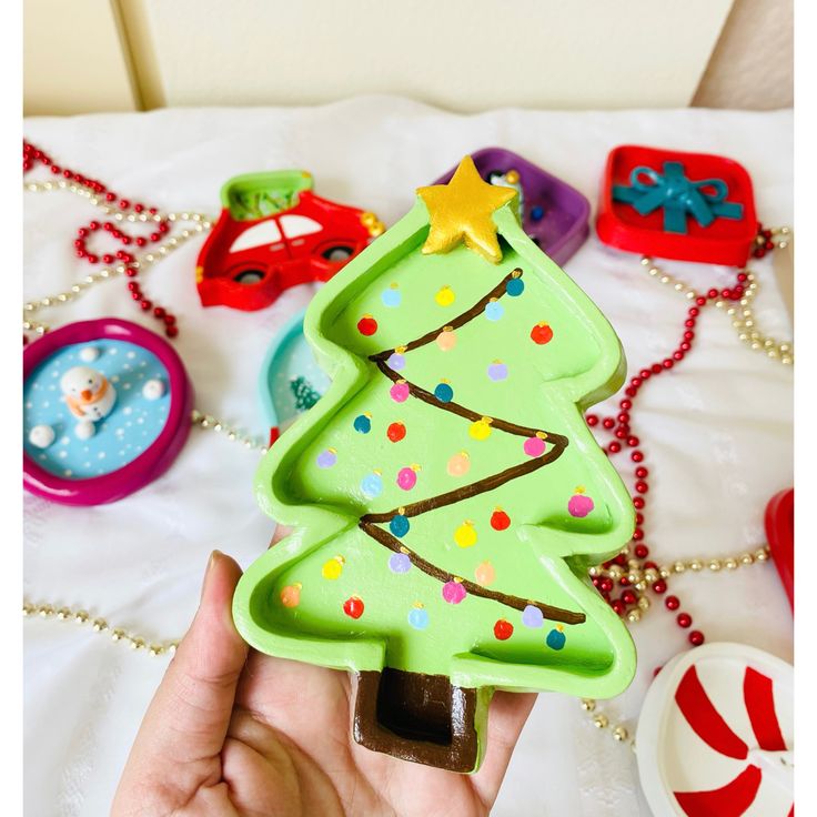 a hand holding a green plastic christmas tree shaped cookie on top of a white table