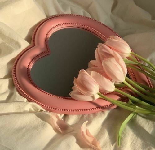 pink tulips in front of a heart shaped mirror on a white bed sheet