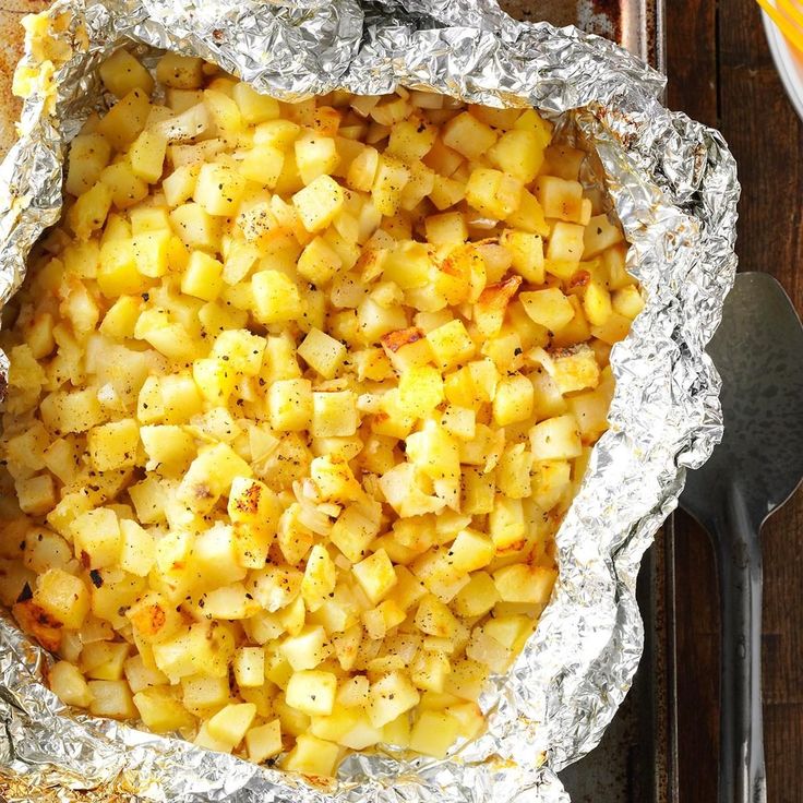 an aluminum foil covered dish with potatoes and seasoning in it on a wooden table