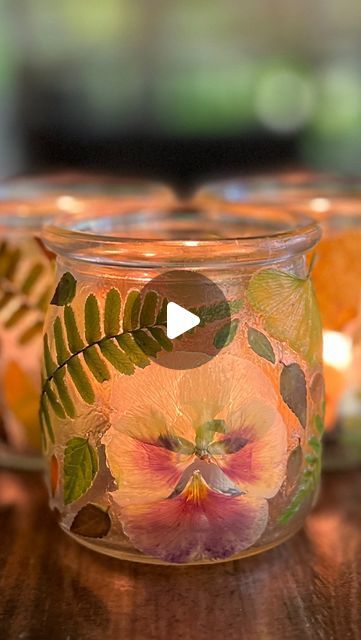 three glass jars filled with flowers and leaves on top of a wooden table next to candles