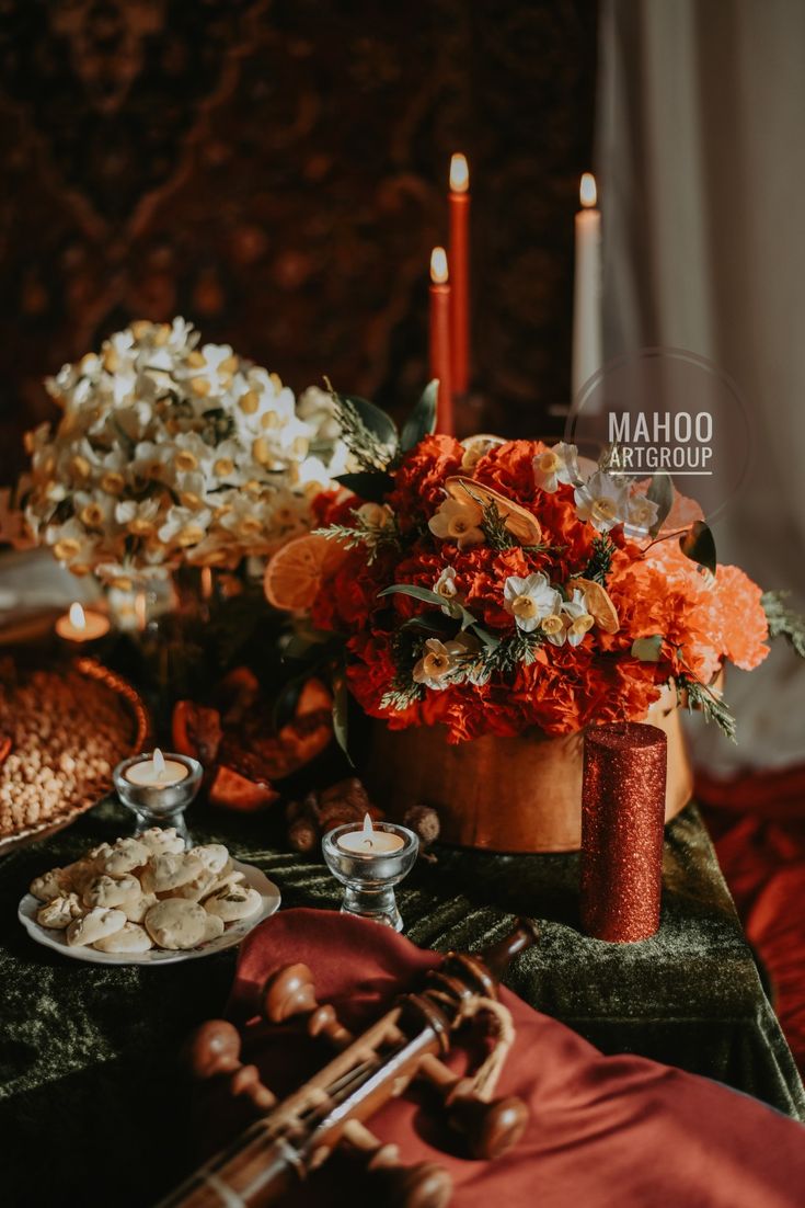 an arrangement of flowers, candles and other items on a table with red cloths