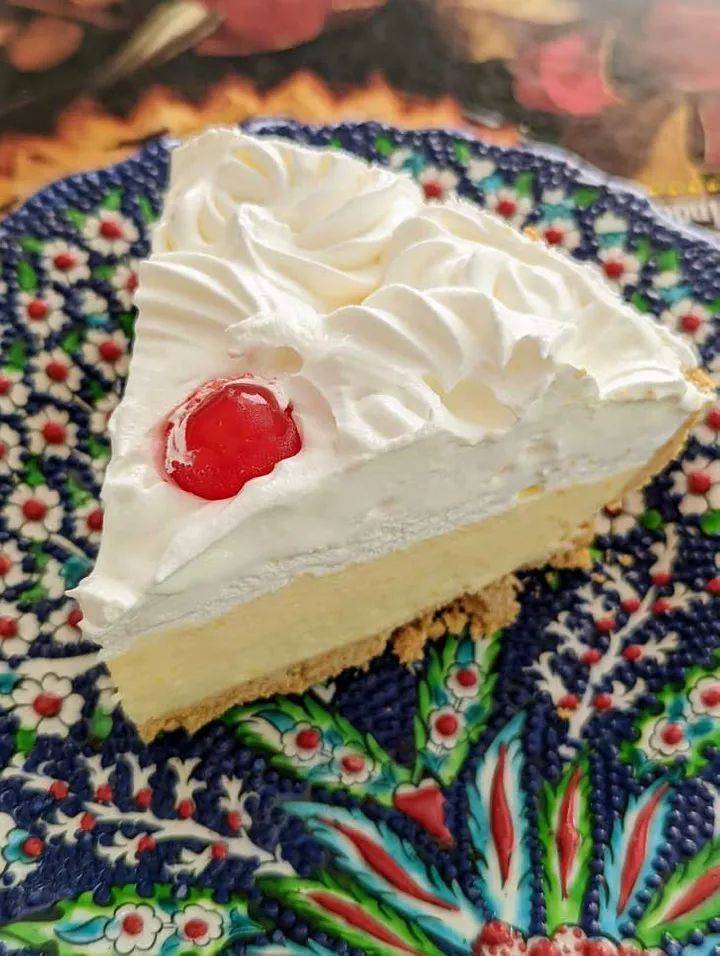 a piece of cheesecake with whipped cream and a cherry on top sitting on a plate