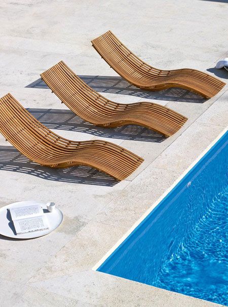 three wooden lounge chairs sitting next to a swimming pool with blue water in the background