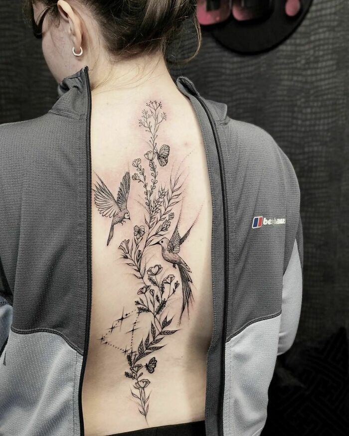 a woman's back tattoo with flowers and birds on her left side ribcage