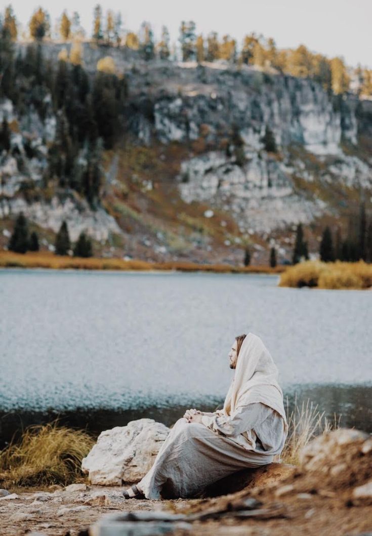 a man sitting on top of a rock next to a lake