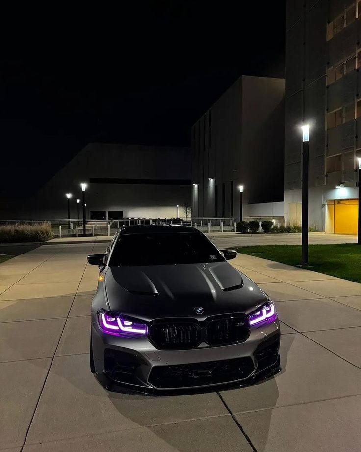 a black car parked in front of a building at night with purple lights on it