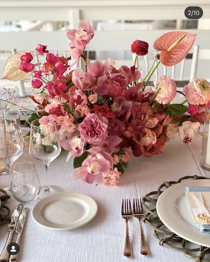 the table is set with pink flowers and silverware, plates and utensils