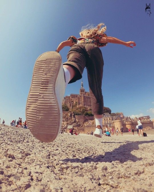 a woman is jumping in the air with her feet up on the sand while people are walking around