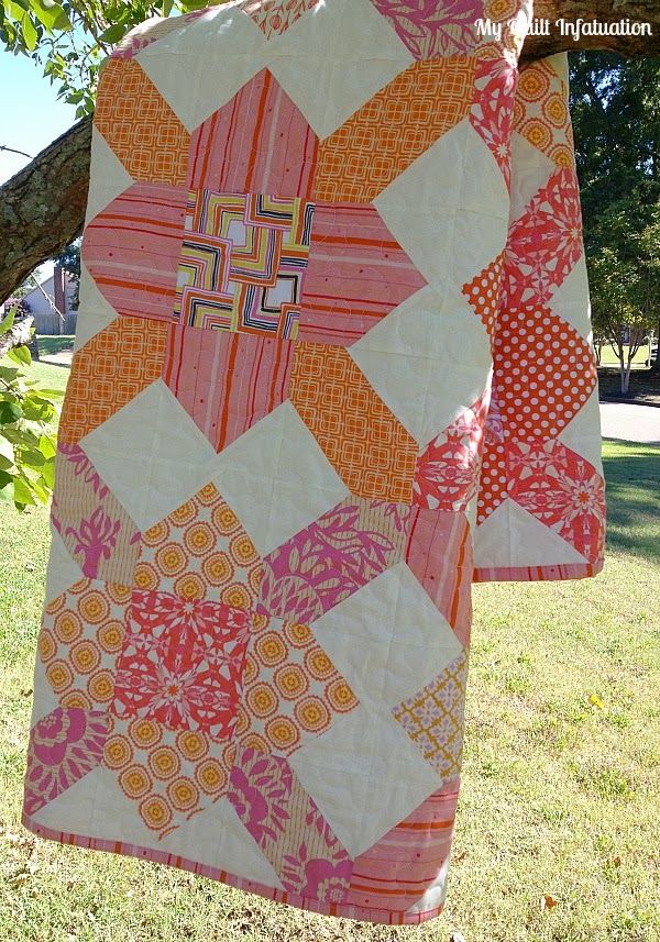 an orange and pink quilt hanging from a tree