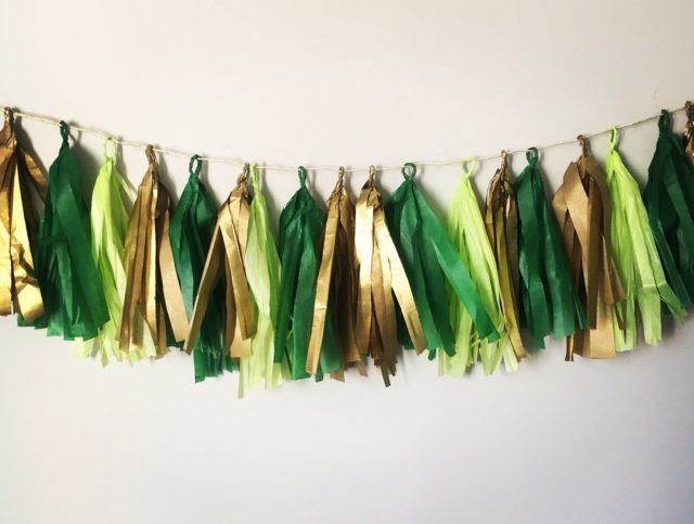 green and gold tissue tassels hanging from a string on a wall in front of a white wall